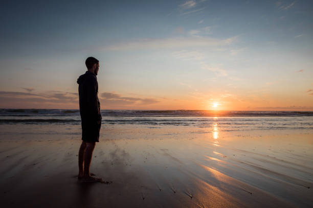 istock young man walking with feet in water on the beach at sunset 1328288366