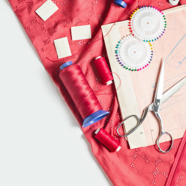 istock Tailor's desk. Pattern of clothes and sewing tools. Red cloth, threads, spools, scissors on a white background 1328288600