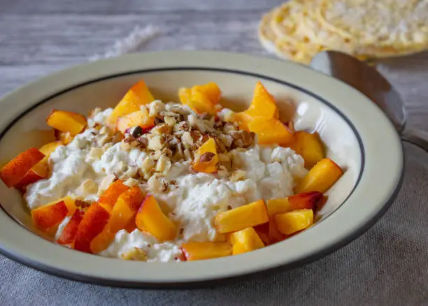 fresh and homemade high protein breakfast with cottage cheese, chopped nectarines and hazelnuts served in a rustic bowl on a table. Front view and closeup