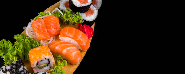 istock Sakes and hosomakis on a wooden plate on a black background. Sushi 1328292408