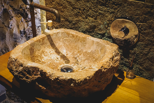 rustic style washbasin made of a stone and the taps made of the same copper pipe. Interior design idea