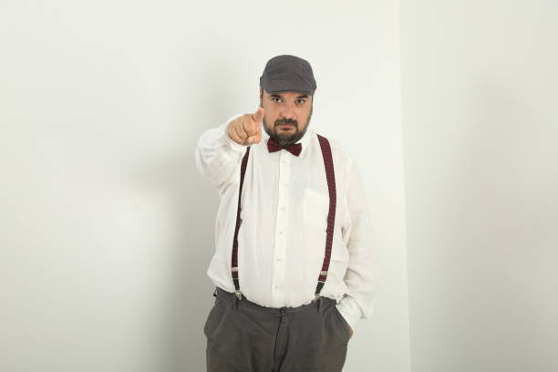 Attractive man with yellow tie, bare feet and black bowler-hat poses to camera, Studio shoot, white background.
