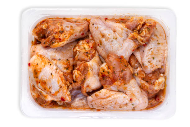Raw spicy chicken wings for grilling in a transparent plastic box isolated on white background \