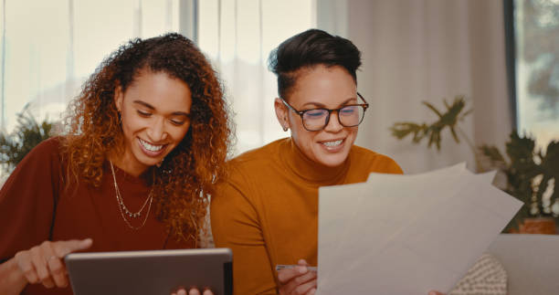 istock Shot of a young lesbian couple doing paperwork while using a digital tablet at home 1328296614