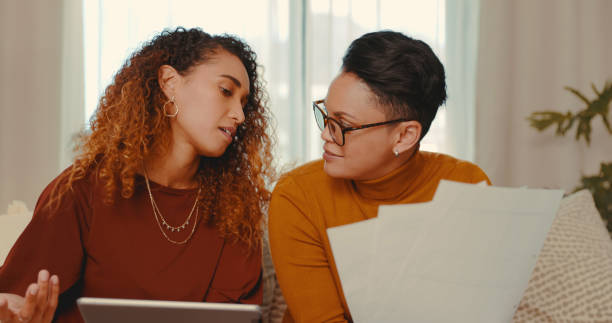 istock Shot of a young lesbian couple doing paperwork while using a digital tablet at home 1328296637