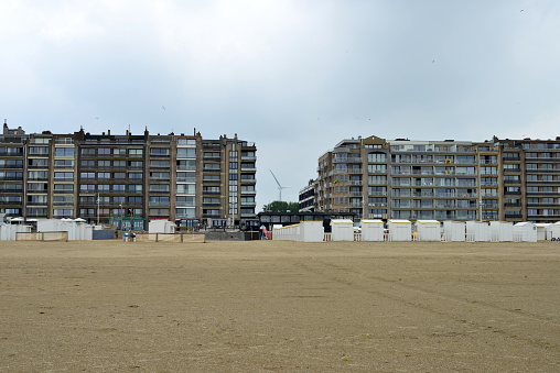 Zeebrugge, Belgium- July 11, 2021: Zeebrugge windturbine wings, terraced apartment facades in front of the beach. National holiday golden spurs, Flemish institution flags are hanging out the windows.