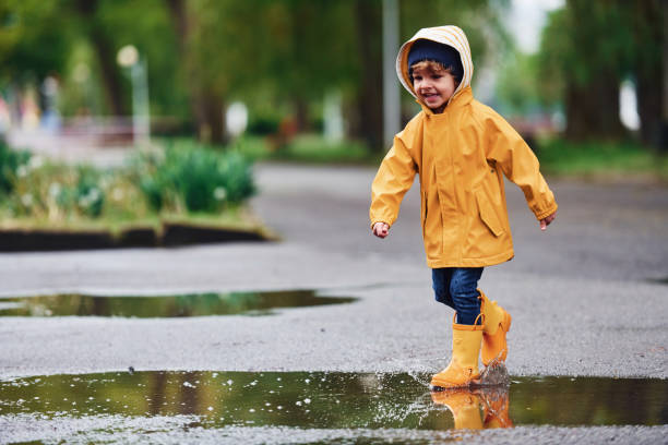 istock Kid in yellow waterproof cloak and boots playing outdoors after the rain 1328300413
