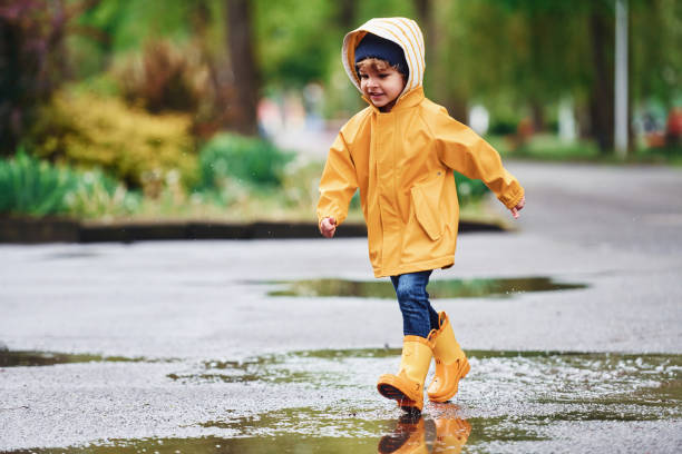 istock Kid in yellow waterproof cloak and boots playing outdoors after the rain 1328300455