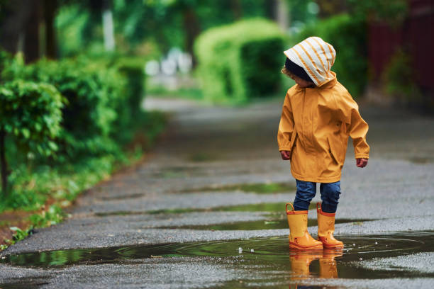 istock Kid in yellow waterproof cloak and boots playing outdoors after the rain 1328300491
