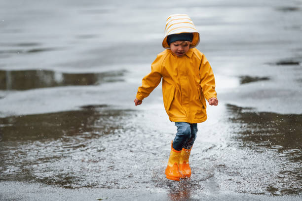 istock Kid in yellow waterproof cloak and boots playing outdoors after the rain 1328300507