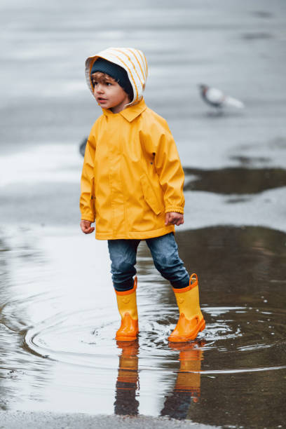 istock Kid in yellow waterproof cloak and boots playing outdoors after the rain 1328300604