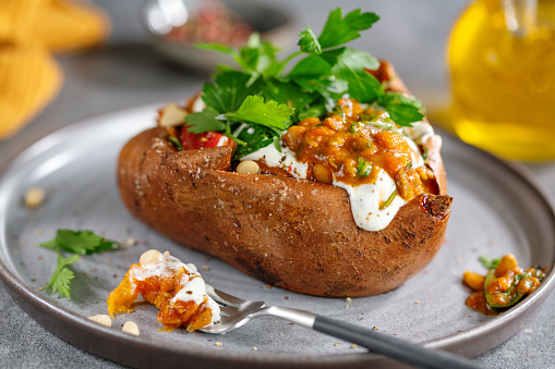 Baked sweet potato with sour cream and beans with parsley served on plate. Closeup.