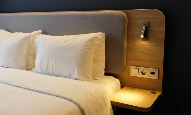 istock Close-up fragment of bedroom with empty bedside table, reading lamp and USB socket in modern interior​ design home or hotel. Soft pillow and blanket, stylish comfortable furniture. 1328303226