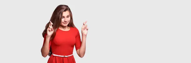 Pretty young woman posing at studio. Banner with copyspace. Sale design. Red dress. Cross finger and pray exam luck. College wishing micacle. Stress emotion. One adorable model