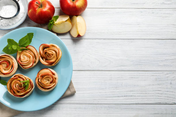 Freshly baked apple roses on white wooden table, flat lay. Space for text