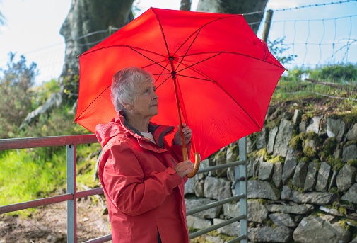 Senior woman with red umbrella outdoors between showers
