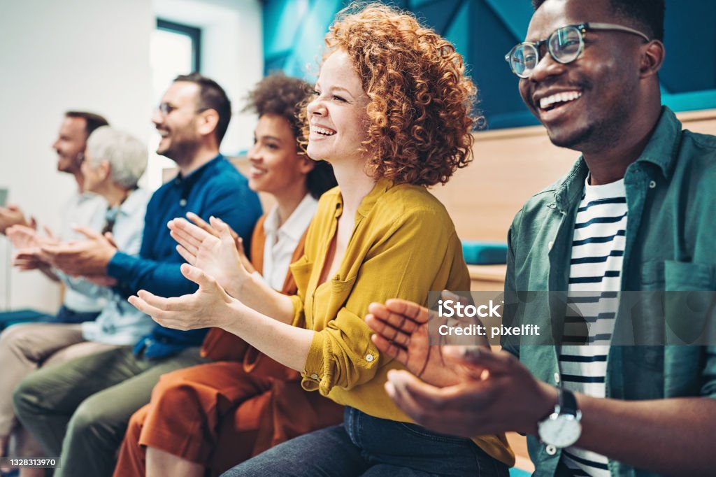 Multi-ethnic group of business persons during a conference Group of people sitting in a row and applauding Multiracial Group Stock Photo