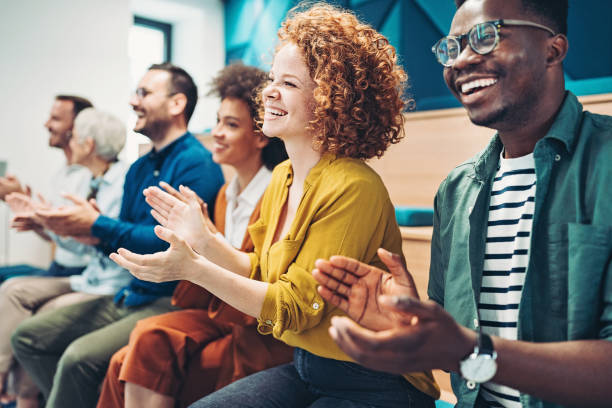 Multi-ethnic group of business persons during a conference Group of people sitting in a row and applauding business conference stock pictures, royalty-free photos & images