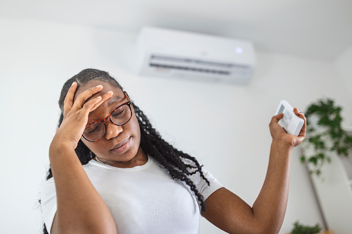 Woman with headache using aircondition unit at home.Conceptual view about health problems caused by exposure to an air conditioner.