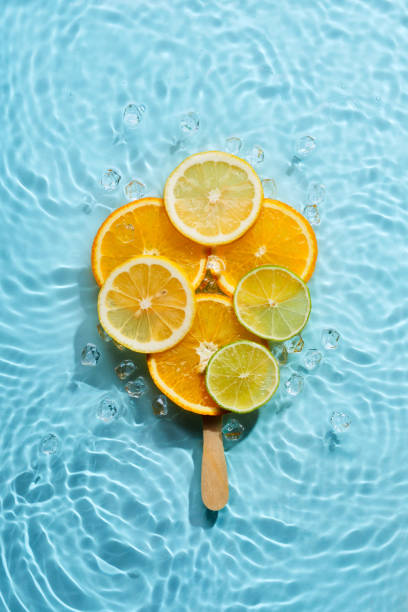 istock Creative ice lolly made from citrus fruit slices in blue water background with concentric circles and ripples. Refreshing summer dessert concept 1328314382
