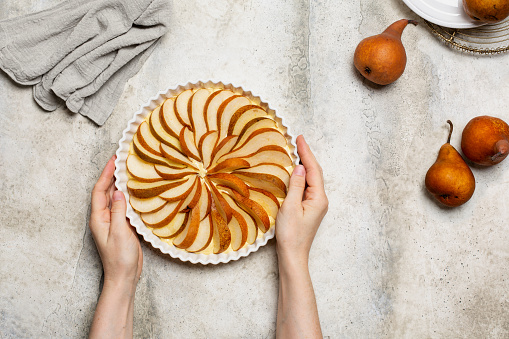 Woman's hands holding a homemade raw pie with fresh  brown pears, before baking. Light background, copy space.