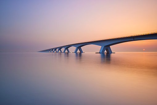 The sun is rising from behind the Zeelandbrug. The bridge goes over a big part of water from one part of the province to the other. The water is very quiet and therefore causes reflection.