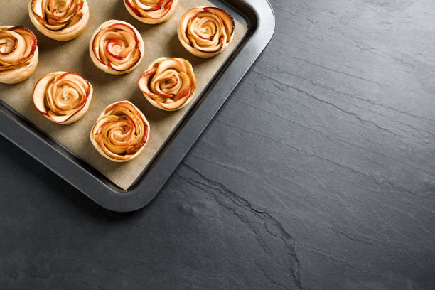 Tray with freshly baked apple roses on black table, top view. Space for text