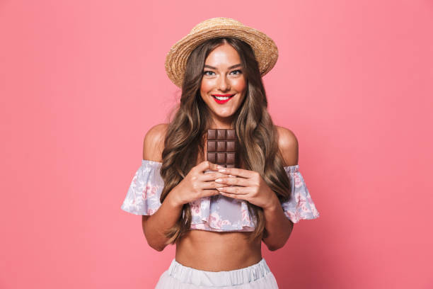 Portrait of a satisfied young girl in summer clothes Portrait of a satisfied young girl in summer clothes holding chocolate bar over pink background isolated color stock pictures, royalty-free photos & images