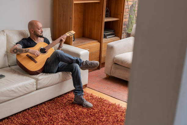 istock Man sitting on his sofa practicing the chords on his guitar while at home alone 1328320818