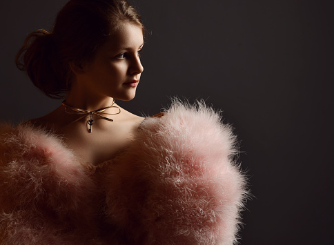 Portrait of royal kid girl theatre actress, ballerina in clothes with big furry sleeves and gold necklace looking aside at copy space over dark background