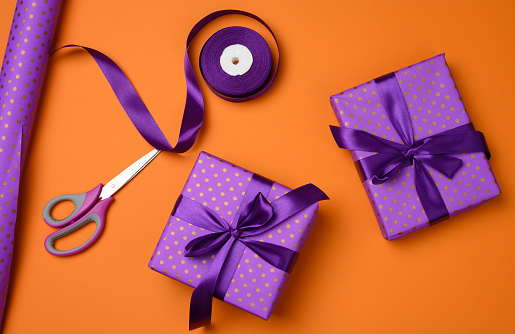 gift boxes tied with purple silk ribbon on an orange background, top view. Festive backdrop, flat lay
