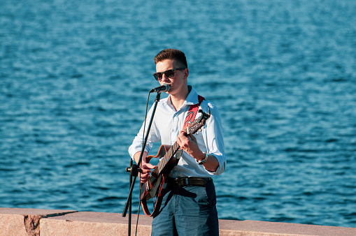 Petrozavodsk, Russia - 13 June 2020. young man plays guitar and sings into microphone on the promenade