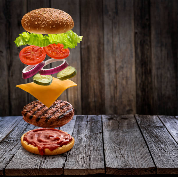 istock Burger layered ingredients as explosion flying open bun on rustic wooden table 1328324359