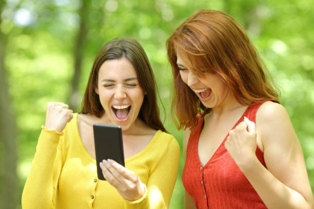istock Two excited women checking smart phone in a park 1328333072