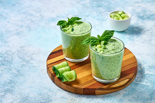 Cucumber Gazpacho - cold summer soup with basil in glasses on wooden board on light background.