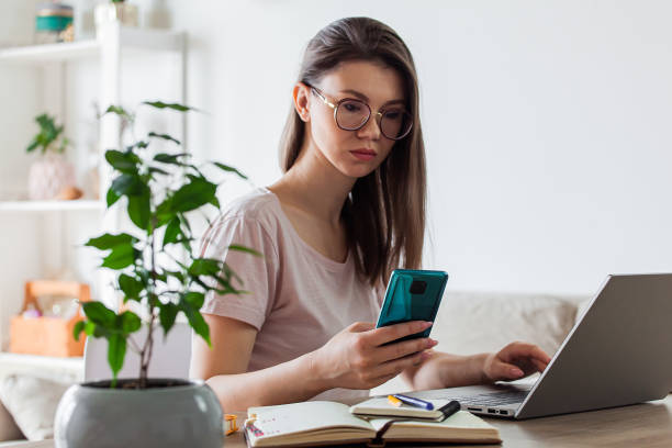 istock Young woman using mobile phone and laptop to work home, multiple devices 1328337546