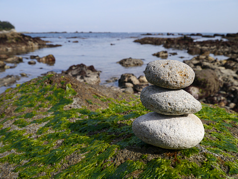 Three stones stacked on a bed of algae overlooking the rocky bay.