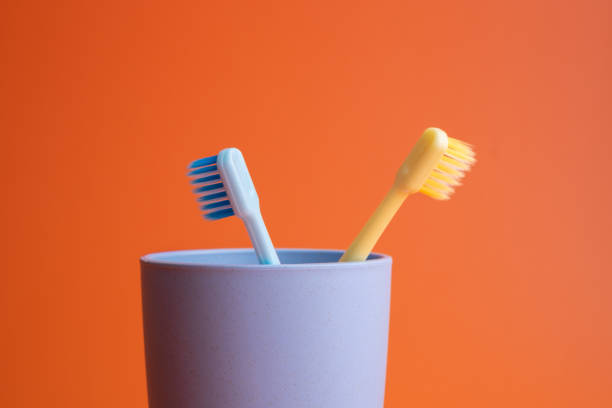 istock Two toothbrushes in plastic cups on orange background 1328341056