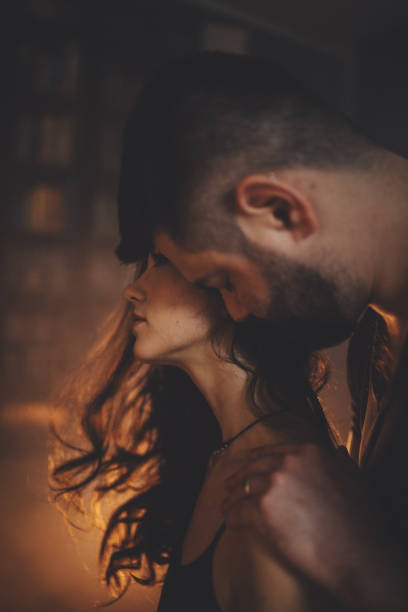 A man hugs a woman from shoulders, view in profile, artificial warm light.