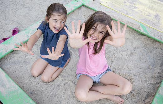 Cheerful little girls sit in the sandbox and play with sand on a hot summer day.