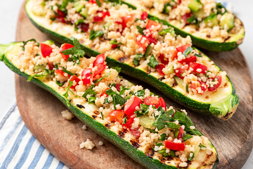 Grilled zucchini stuffed with couscous, tomatoes, cucumber and parsley. Vegan stuffed zucchini on a cutting board. Vegetarian food.