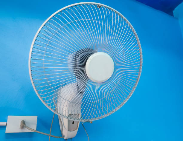 White electric fan is mounted on a blue cement wall.