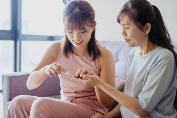 une femme asiatique aide sa mère à vérifier le taux de sucre dans le sang à la maison - kit mains libres photos et images de collection