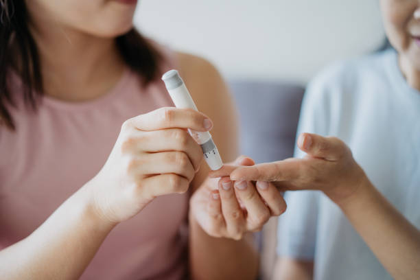 Close-up woman helping her mother check blood sugar level using a blood glucose meter at home Image of an Asian Chinese woman helping her mother check blood sugar level using a blood glucose meter at home blood sugar test stock pictures, royalty-free photos & images