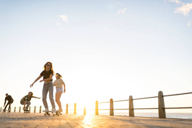 Young skateboarders riding along beach promenade at sunset