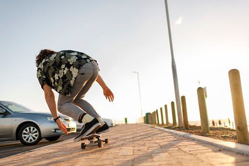 Young man skateboarding down promenade at sunset
