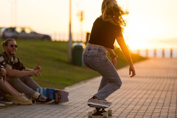 istock Back view young woman doing tricks skateboarding past friends 1328346047