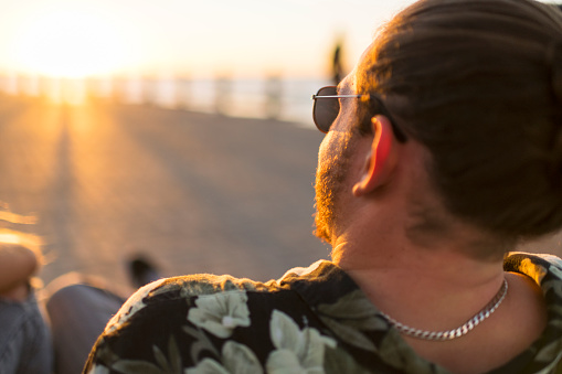 Back view young man with beard and hair bun wearing sunglasses looking to sunset