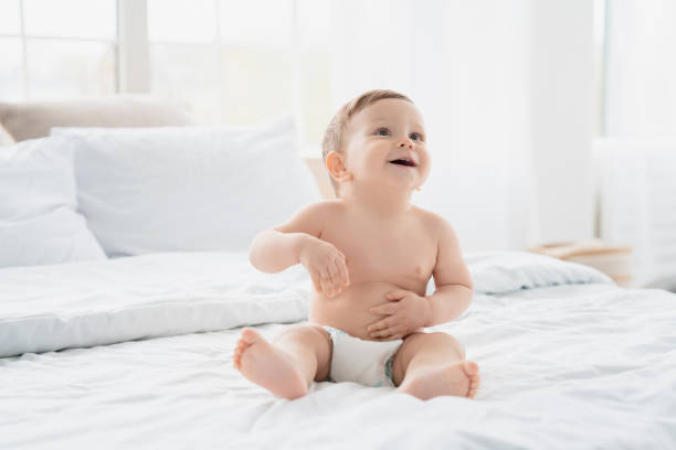 cute small little newborn baby wearing a diaper sitting on white blanket in nursery bed. child kid after bath shower. infant daughter son nappy change and skin care. childhood concept - people purity personal accessory handkerchief imagens e fotografias de stock