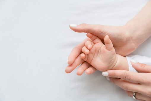 Imagen de cerca de la mano de la mamá de una madre sosteniendo la pequeña mano recién nacida de su pequeño niño sobre fondo blanco. Cuidado de los hijos, concepto de maternidad. photo